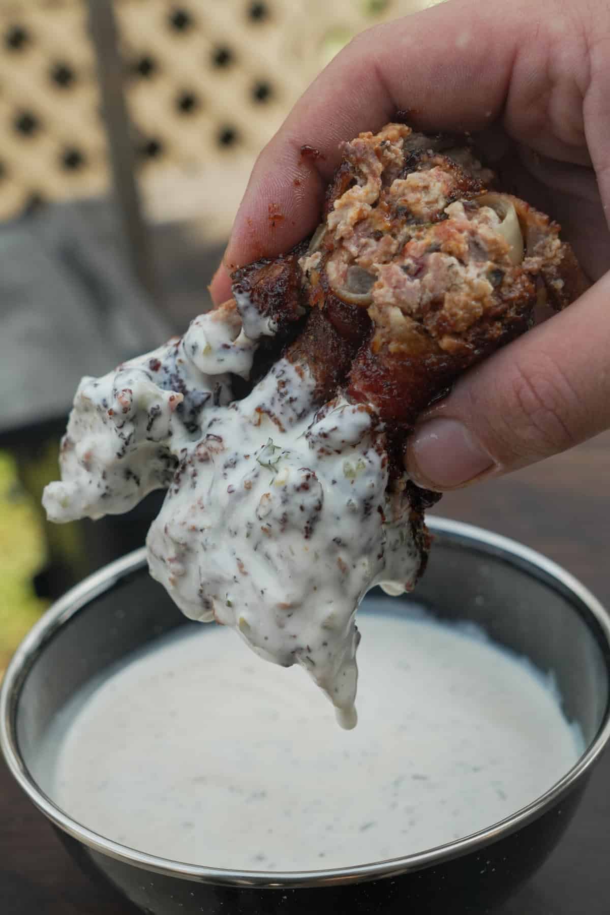 A hand holding a sliced Texas Twinkie stuffed onion ring and dipping it in sauce