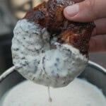 A hand holding a Texas Twinkie stuffed onion ring and dipping it in a bowl of white sauce