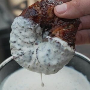 A hand holding a Texas Twinkie stuffed onion ring and dipping it in a bowl of white sauce