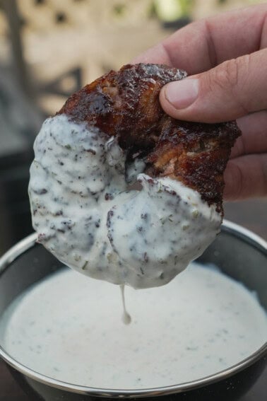 A hand holding a Texas Twinkie stuffed onion ring and dipping it in a bowl of white sauce