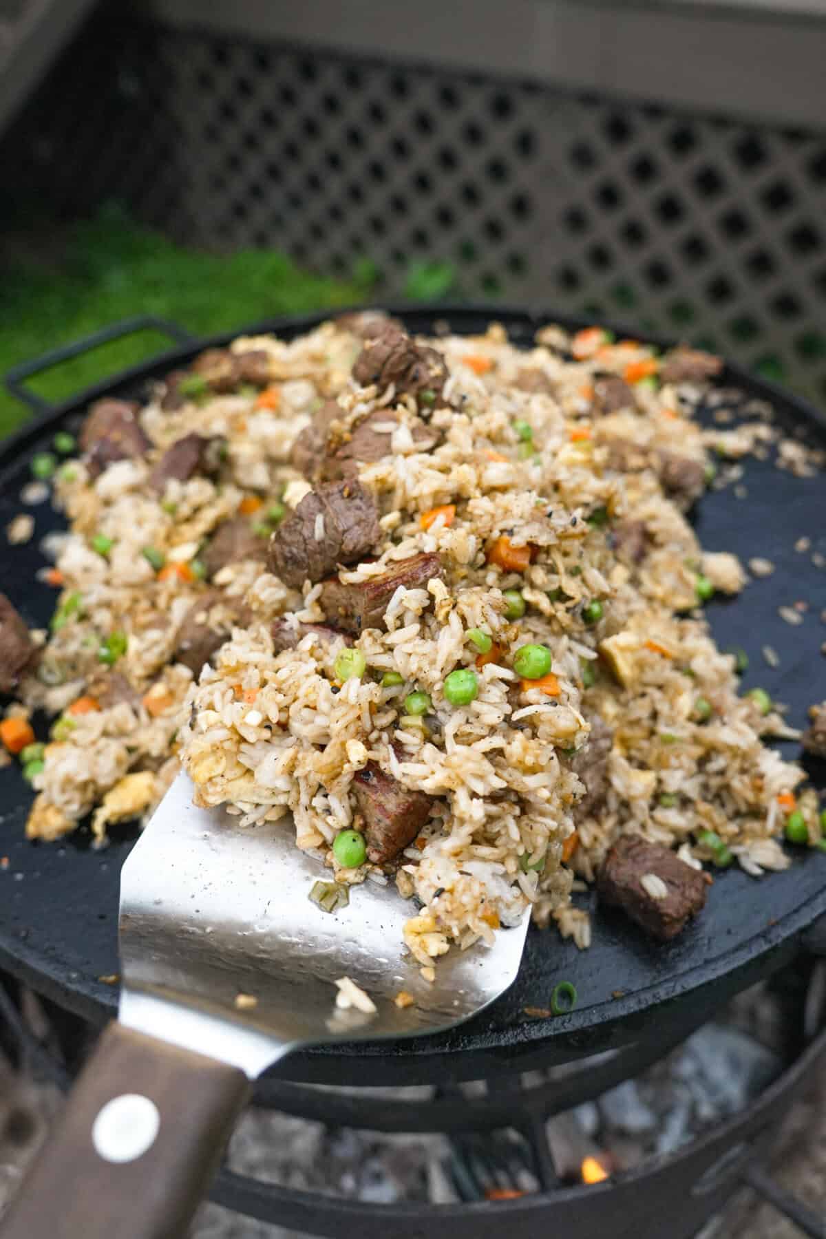 A spatula scooping a portion of steak fried rice off a plate