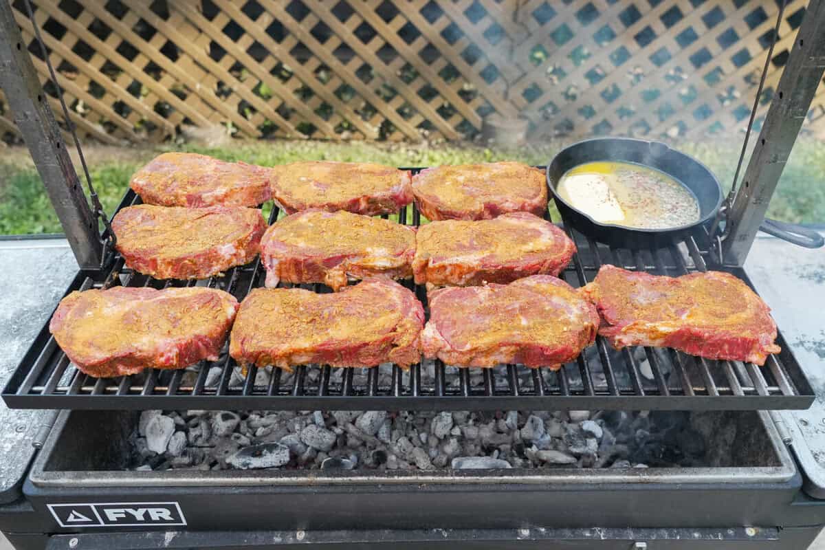 A FYR Grill filled with seasoned steaks and bourbon butter in a cast iron skillet in the top corner