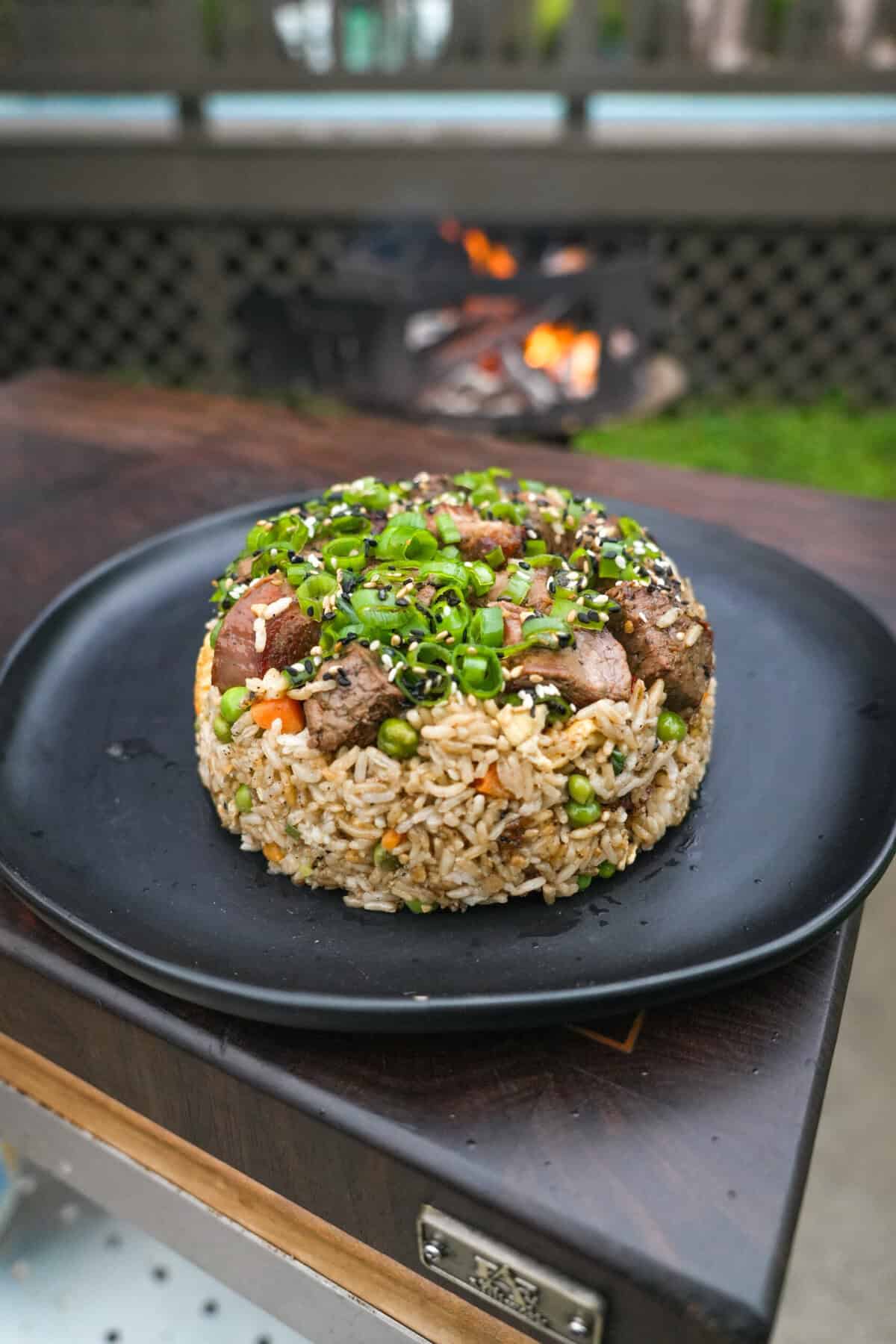 A plate of steak fried rice with peas, carrots, eggs and garnished with scallion greens, sesame seeds and yum yum sauce