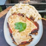 A plate of chicken Parmesan, with breaded chicken topped with marinara tomato sauce, melted browned mozzarella cheese, fresh basil and rigatoni alfredo on the side