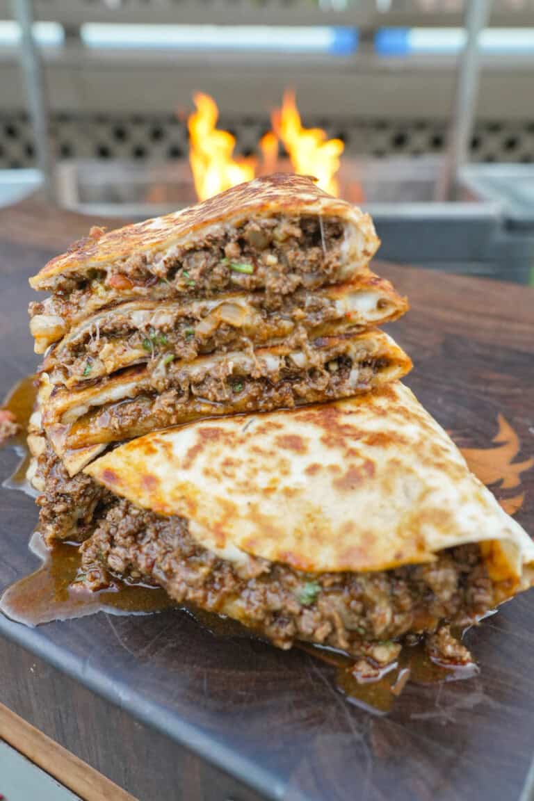 A stack of sliced venison quesadillas with ground venison, mozzarella cheese and tortillas with a grill fire in the background
