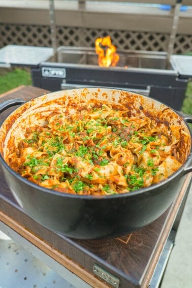 A finished pot of braised beef ragu, tossed with pasta and garnished with chopped parsley and Parmesan cheese