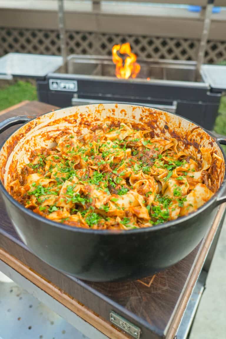 A finished pot of braised beef ragu, tossed with pasta and garnished with chopped parsley and Parmesan cheese
