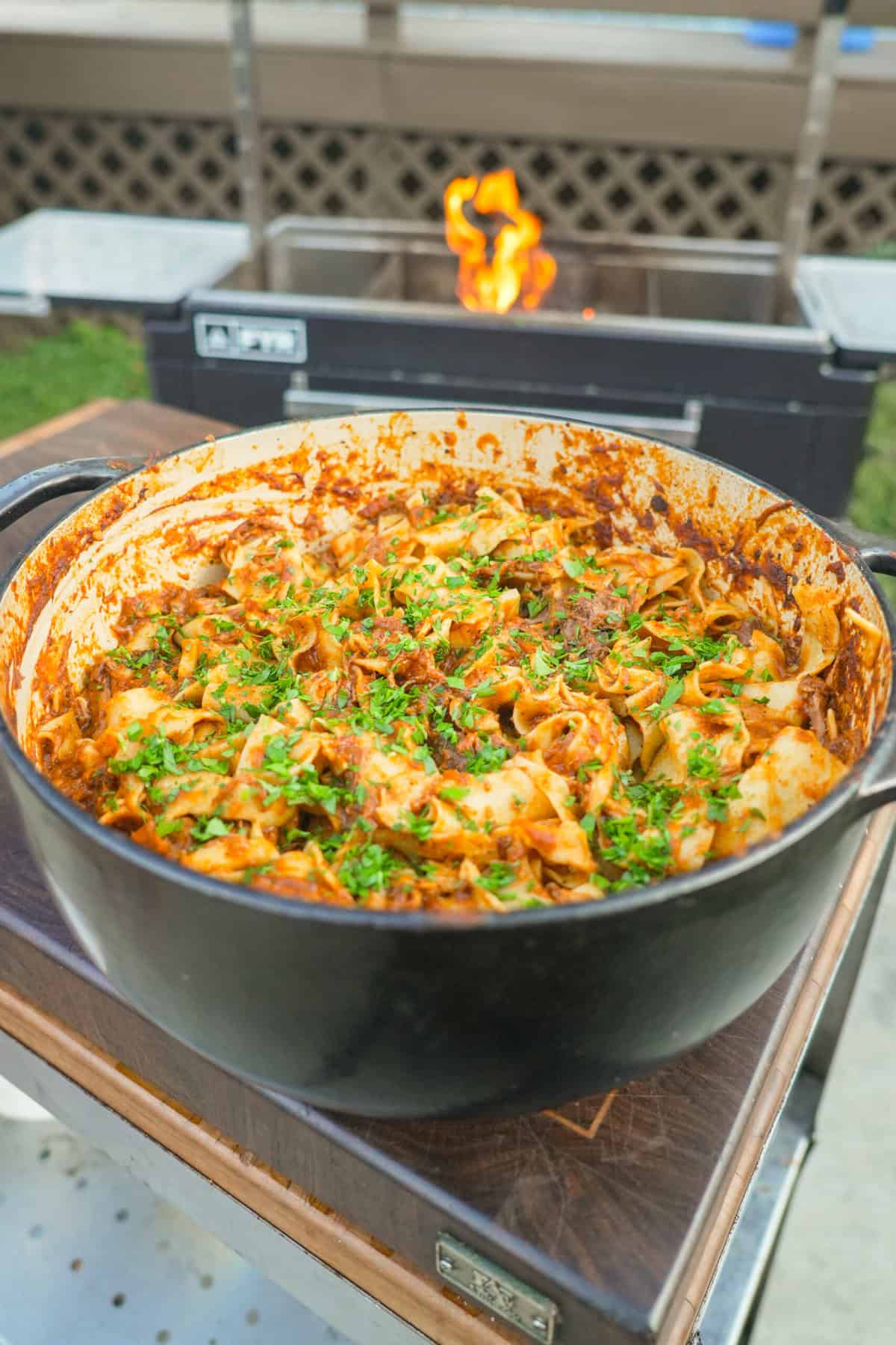 A finished pot of braised beef ragu, tossed with pasta and garnished with chopped parsley and Parmesan cheese