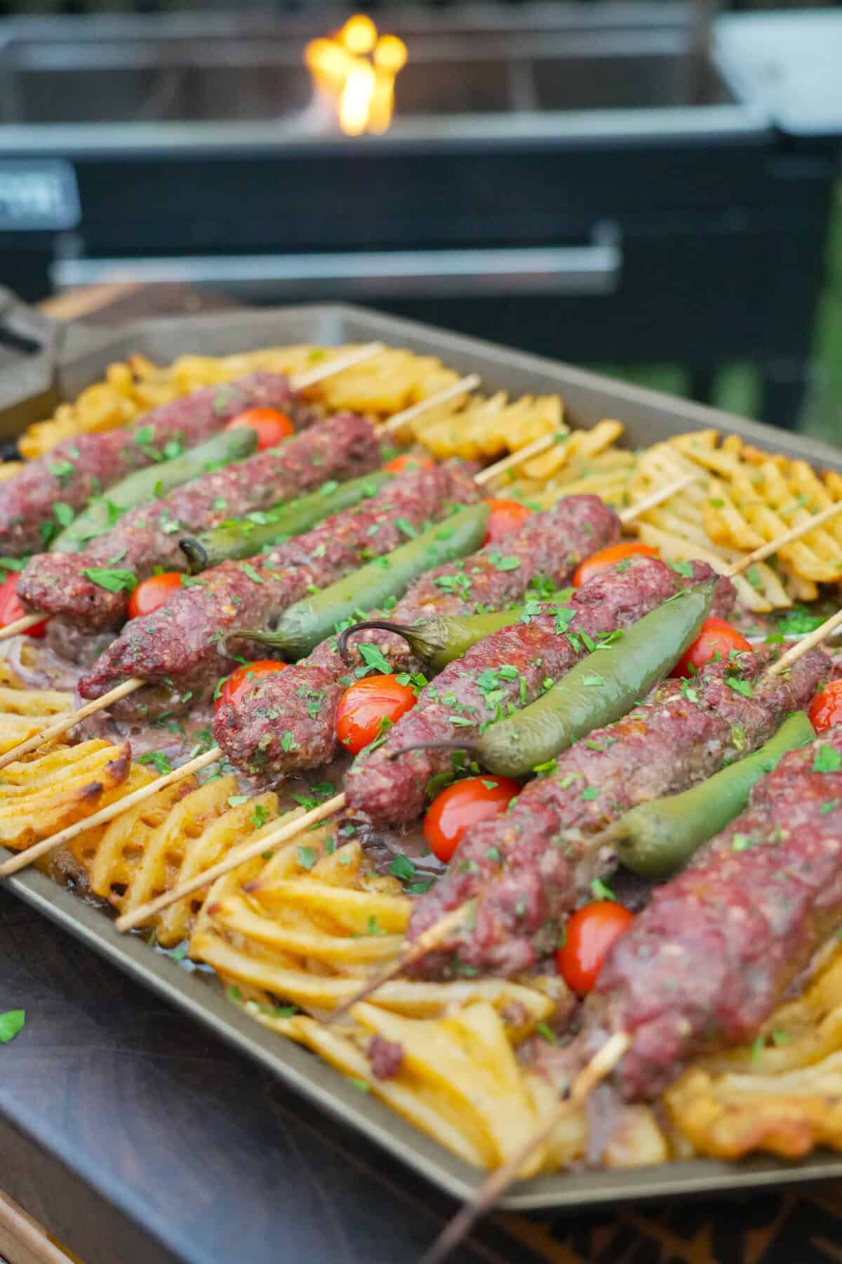 A close up of the finished dish, complete with cooked waffle fries, sliced onions, cherry tomatoes and chile peppers