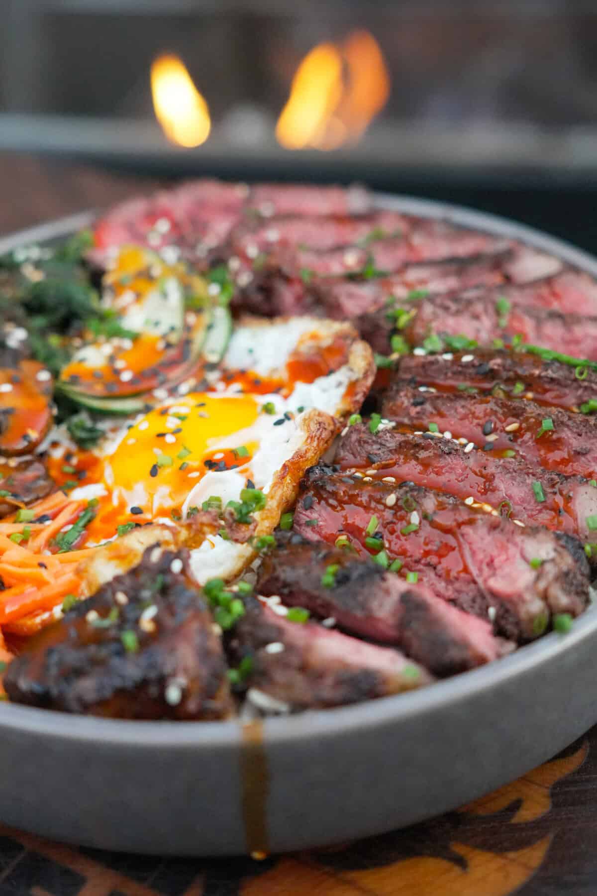 A close up of bowl of steak bibimbap, with grilled ribeye, a fried egg, gochujang sauce and seasoned vegetables