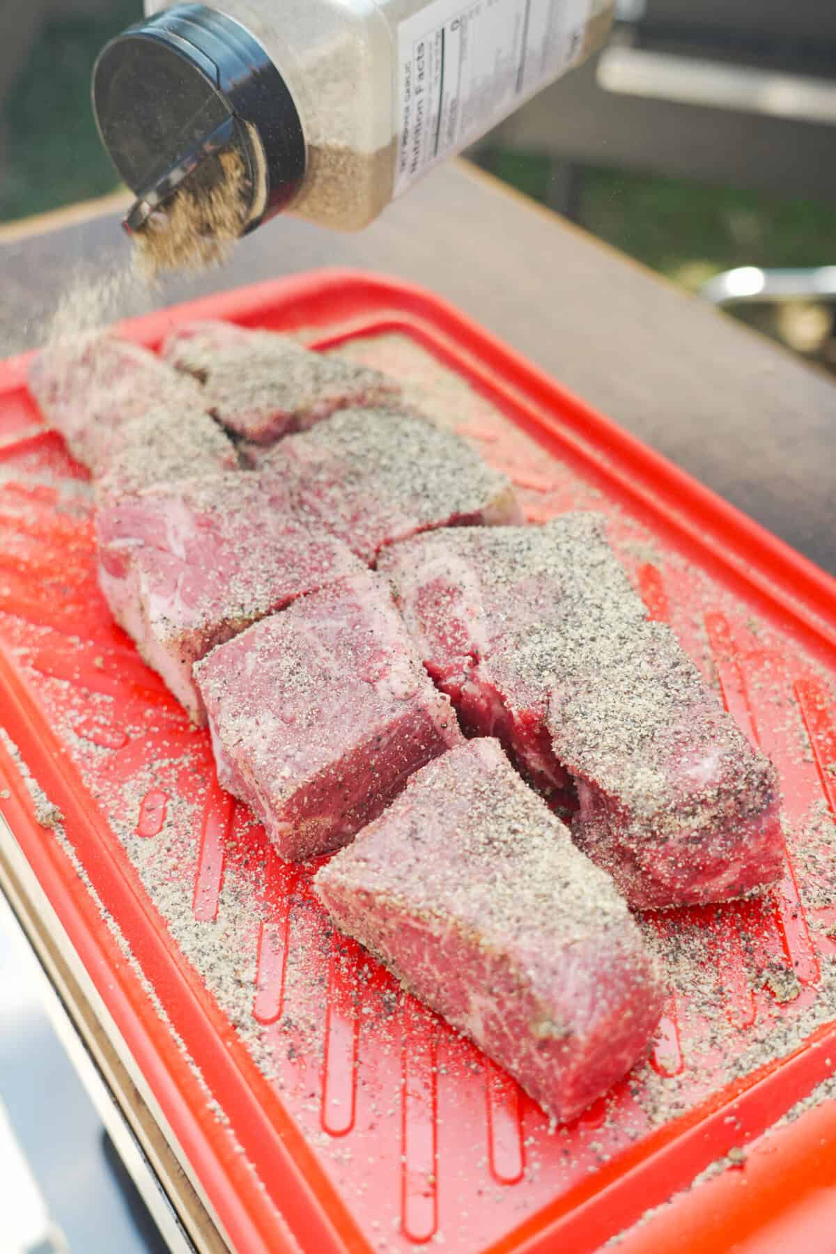 Seasoning pieces of chuck roast with kosher salt, black pepper and garlic powder