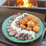A platter of grilled New York strip steak with jalapeño popper croquettes and avocado ranch dressing in between them