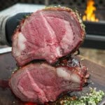 A close up of sliced hot honey smoked prime rib with a grill fire in the background