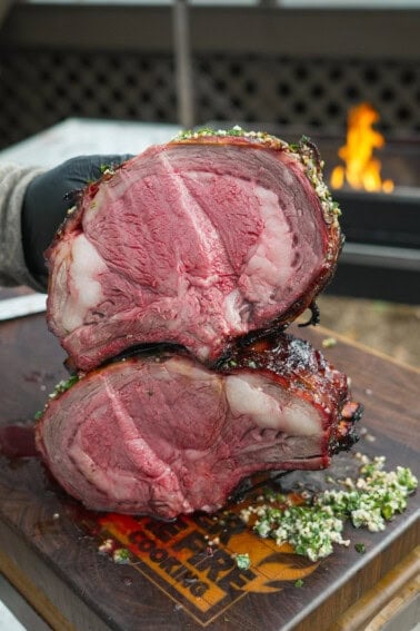 A close up of sliced hot honey smoked prime rib with a grill fire in the background