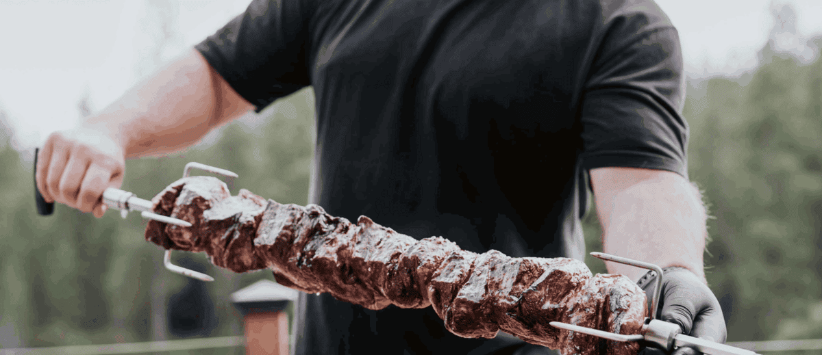 A man holding grilled meat threaded on a rotisserie