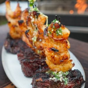 A row of hot honey steak and shrimp on a plate, with filet mignon as the base and shrimp skewers stacked on top of the steak