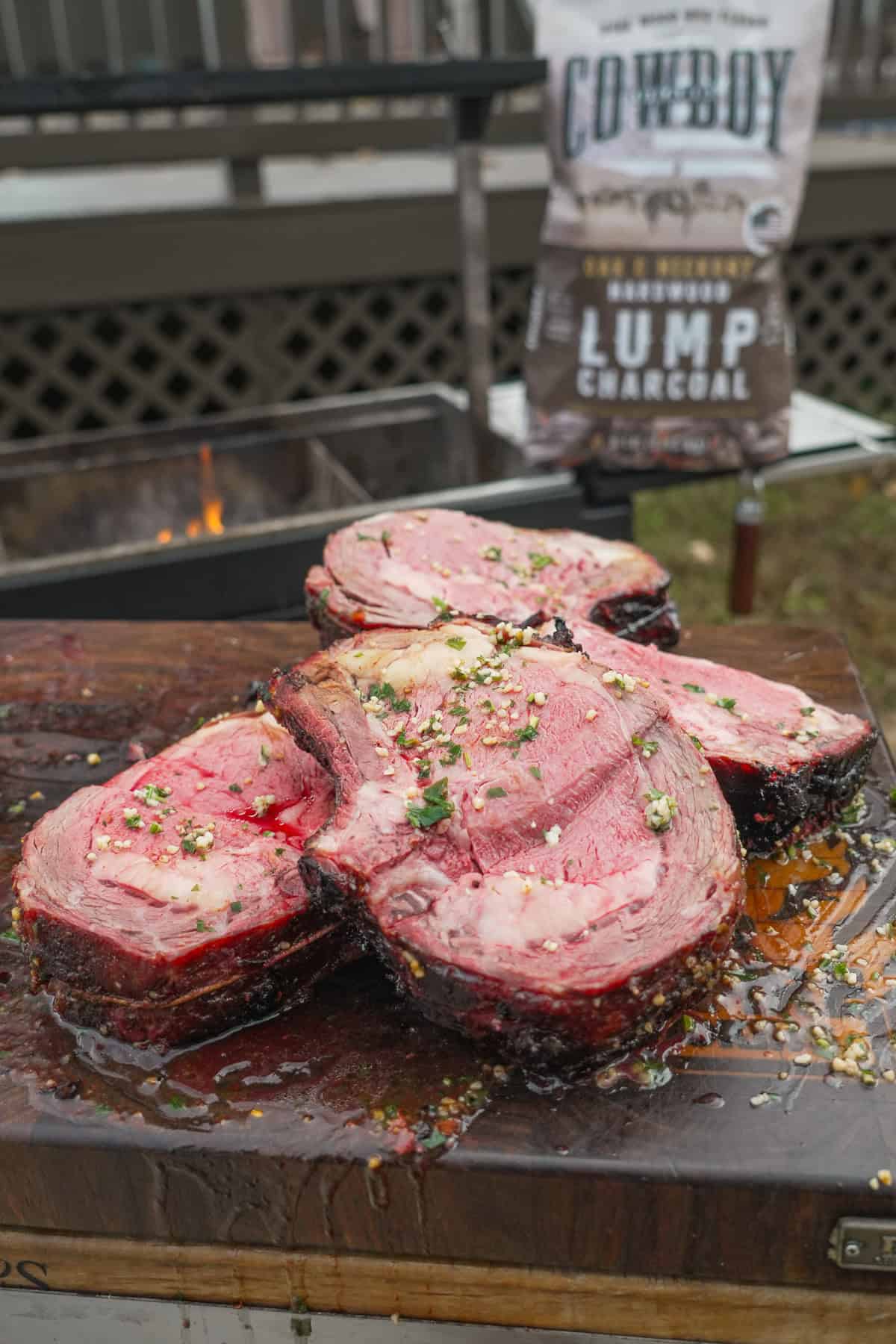Sliced pieces of prime rib roast with herb butter and a bag of Cowboy Charcoal in the background
