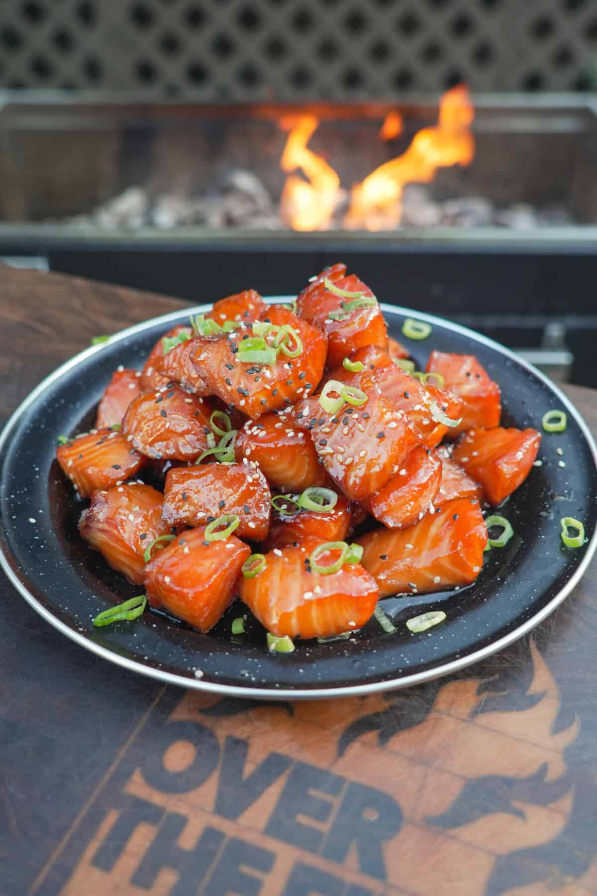 A finished plate of smoked salmon burnt ends, glazed with honey sriracha sauce and garnished with scallions and sesame seeds
