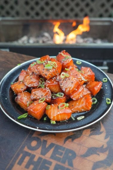 A finished plate of smoked salmon burnt ends, glazed with honey sriracha sauce and garnished with scallions and sesame seeds