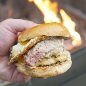 A hand holding a steak and egg burger, with ground beef patties and chimichurri aioli