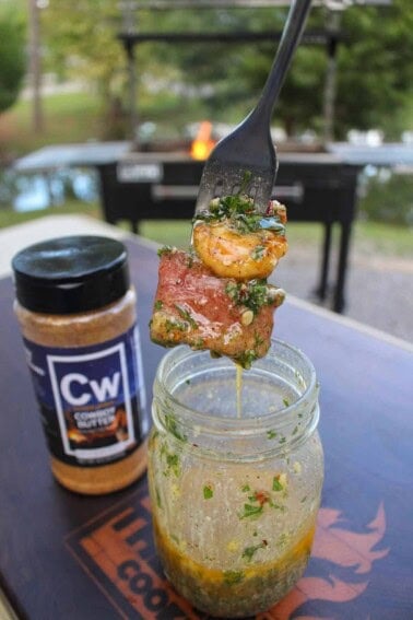 A forkful of steak and shrimp, held above a mason jar filled with cowboy butter and Cowboy Butter Seasoning jar in the background