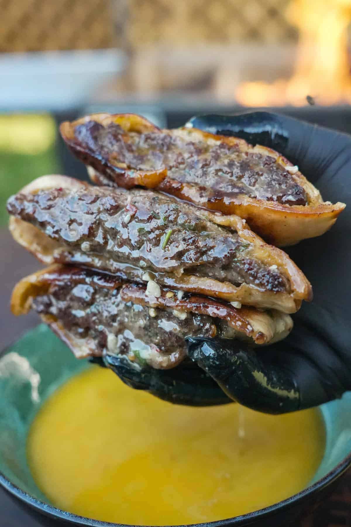 A gloved hand holding a stack of steak arayes over a bowl of cowboy butter
