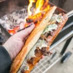 Close-up of a steak sandwich being grilled over an open flame, showcasing deliciously cooked beef, melted cheese, and toasted bread.