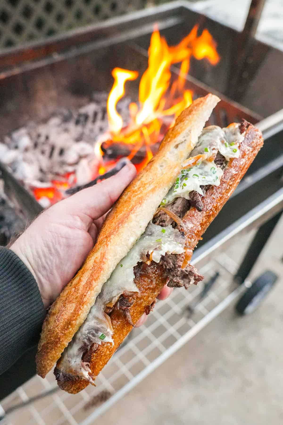 Close-up of a French dip sandwich that was grilled over an open flame, showing deliciously cooked beef, melted cheese, and toasted bread.