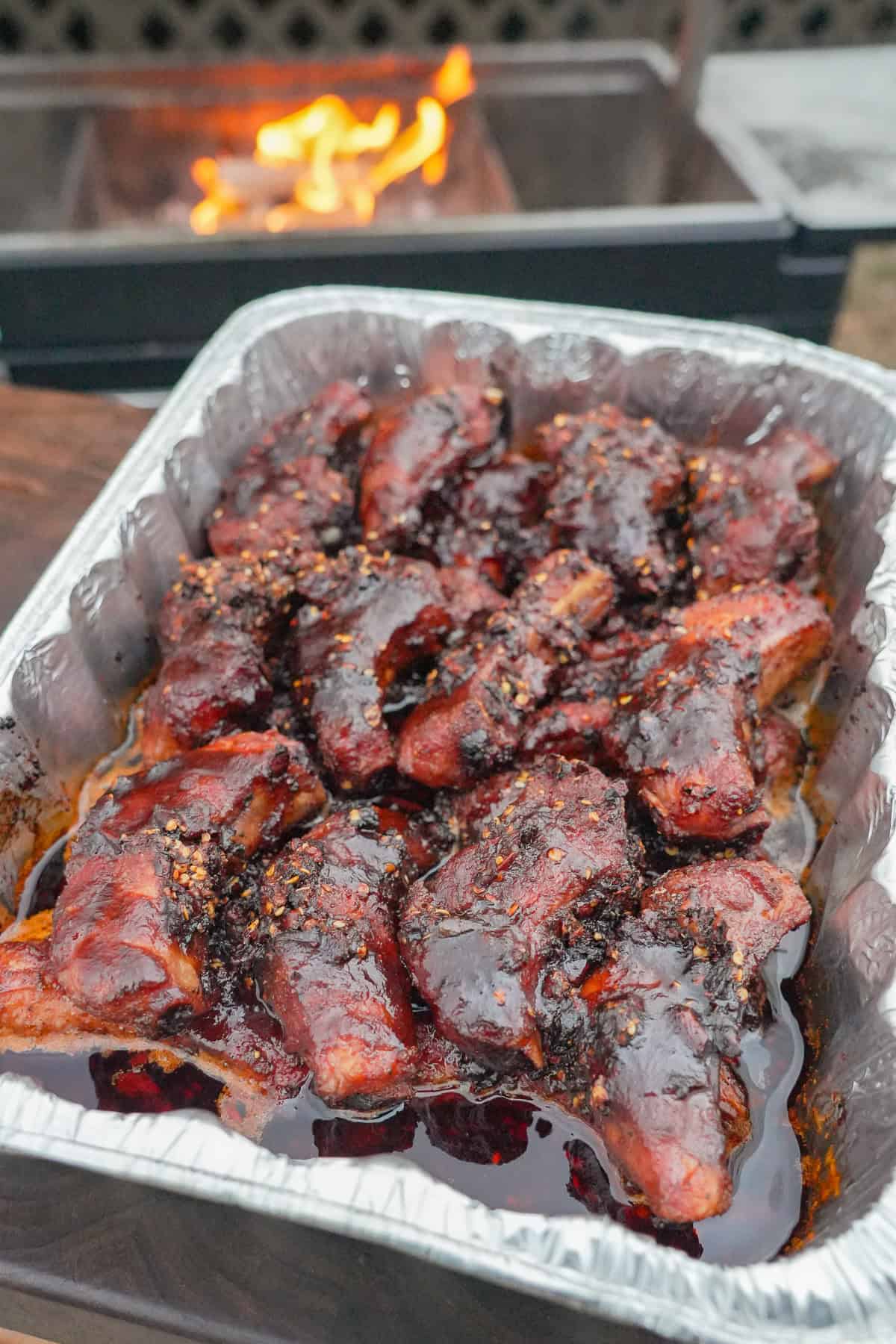 A close up of individual ribs in a foil pan for the crutch, with butter, BBQ sauce, honey and chili oil