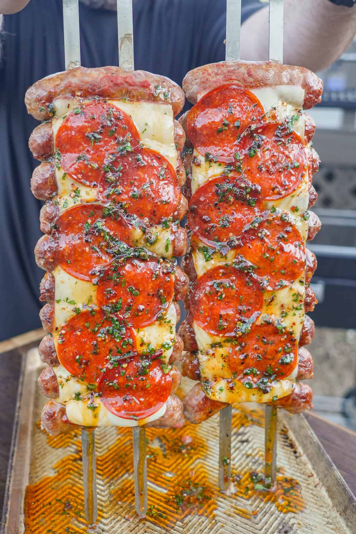 A close up shot of hot honey pizza sausage skewers, with sausage on skewers and pizza sauce, mozzarella cheese, pepperoni and fresh basil on top