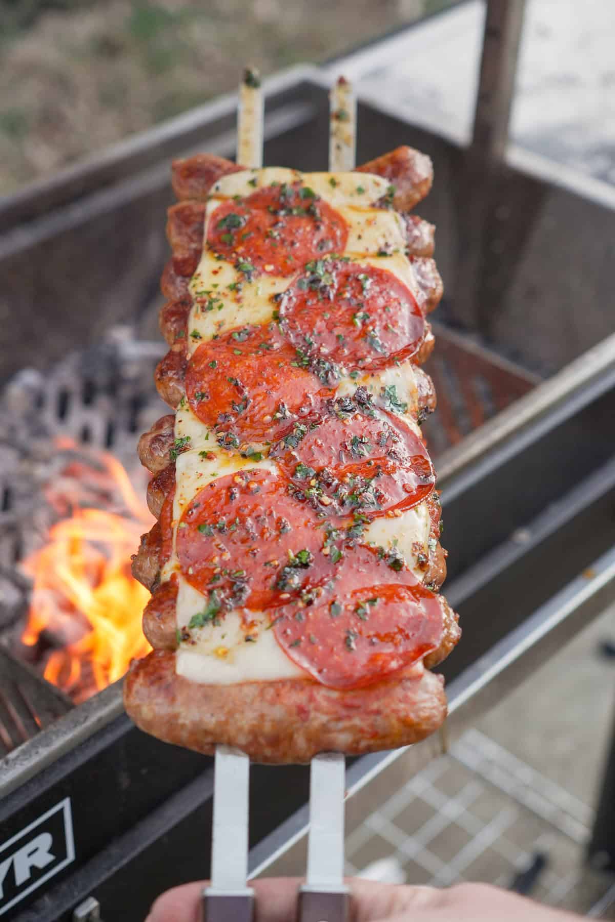 Derek Wolf holding a cooked hot honey pizza sausage skewer with the grill in the background