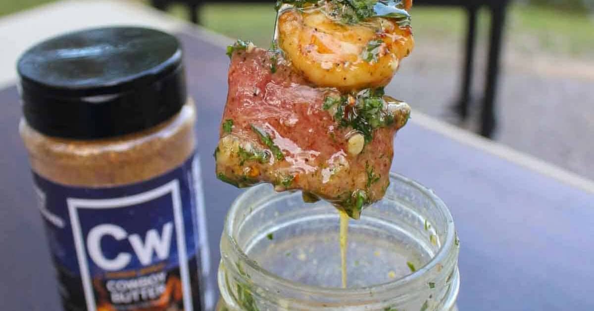 A forkful of steak and shrimp above a mason jar filled with cowboy butter, with a jar of Cowboy Butter Seasoning in the background