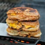 A stack of croissant three smashburgers on a cast iron skillet over the grill