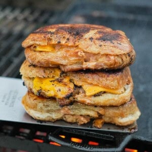 A stack of croissant three smashburgers on a cast iron skillet over the grill