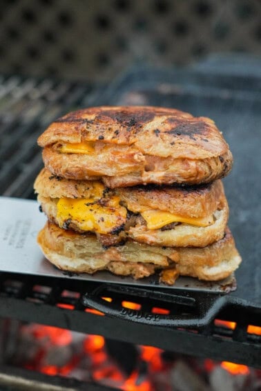 A stack of croissant three smashburgers on a cast iron skillet over the grill