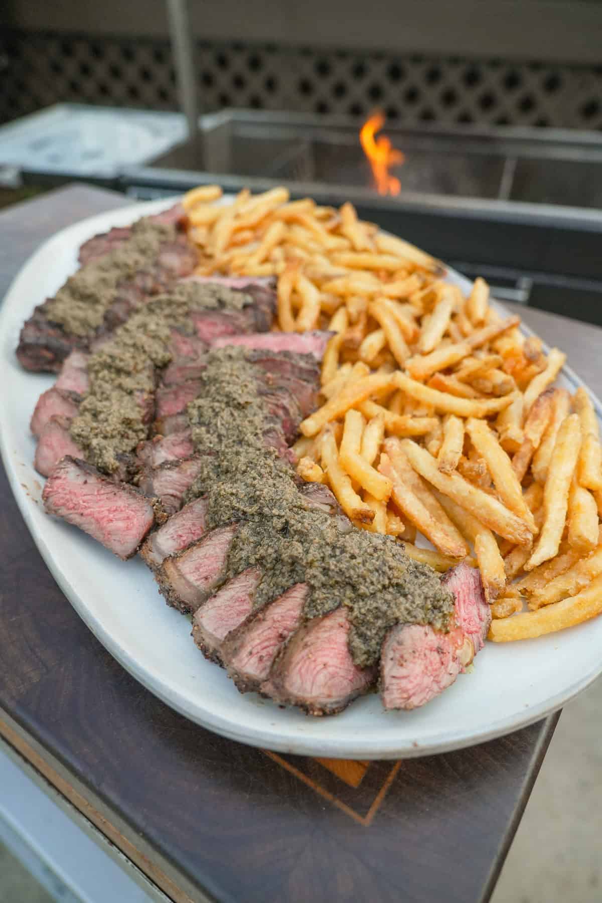 A full platter of French steak frites, with sliced steak and crispy fries topped with Le Relais de Venise sauce