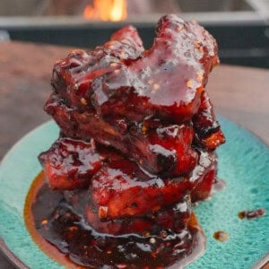 A stack of glazed, caramelized honey chili oil party ribs on a plate in front of the grill