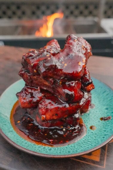 A stack of glazed, caramelized honey chili oil party ribs on a plate in front of the grill