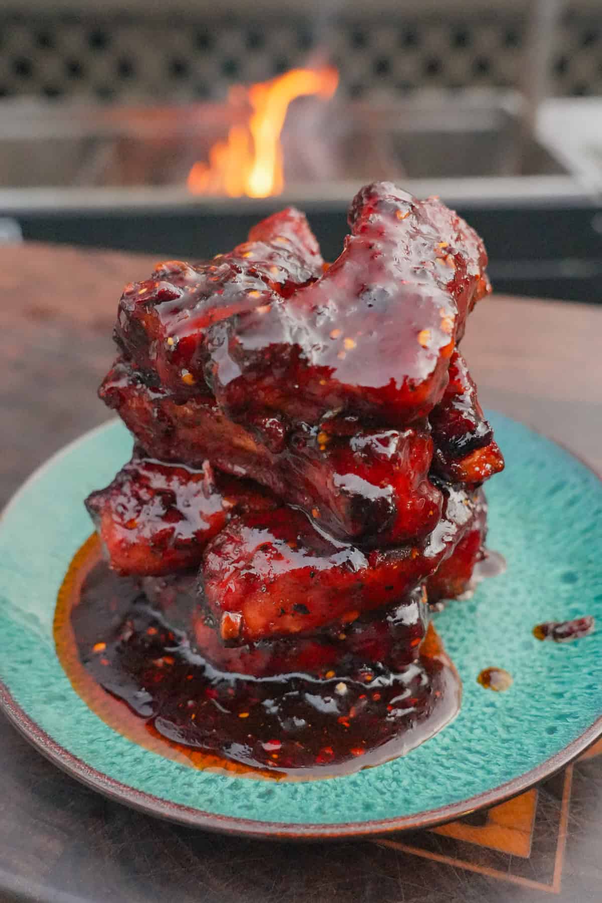 A stack of glazed, caramelized honey chili oil party ribs on a plate in front of the grill