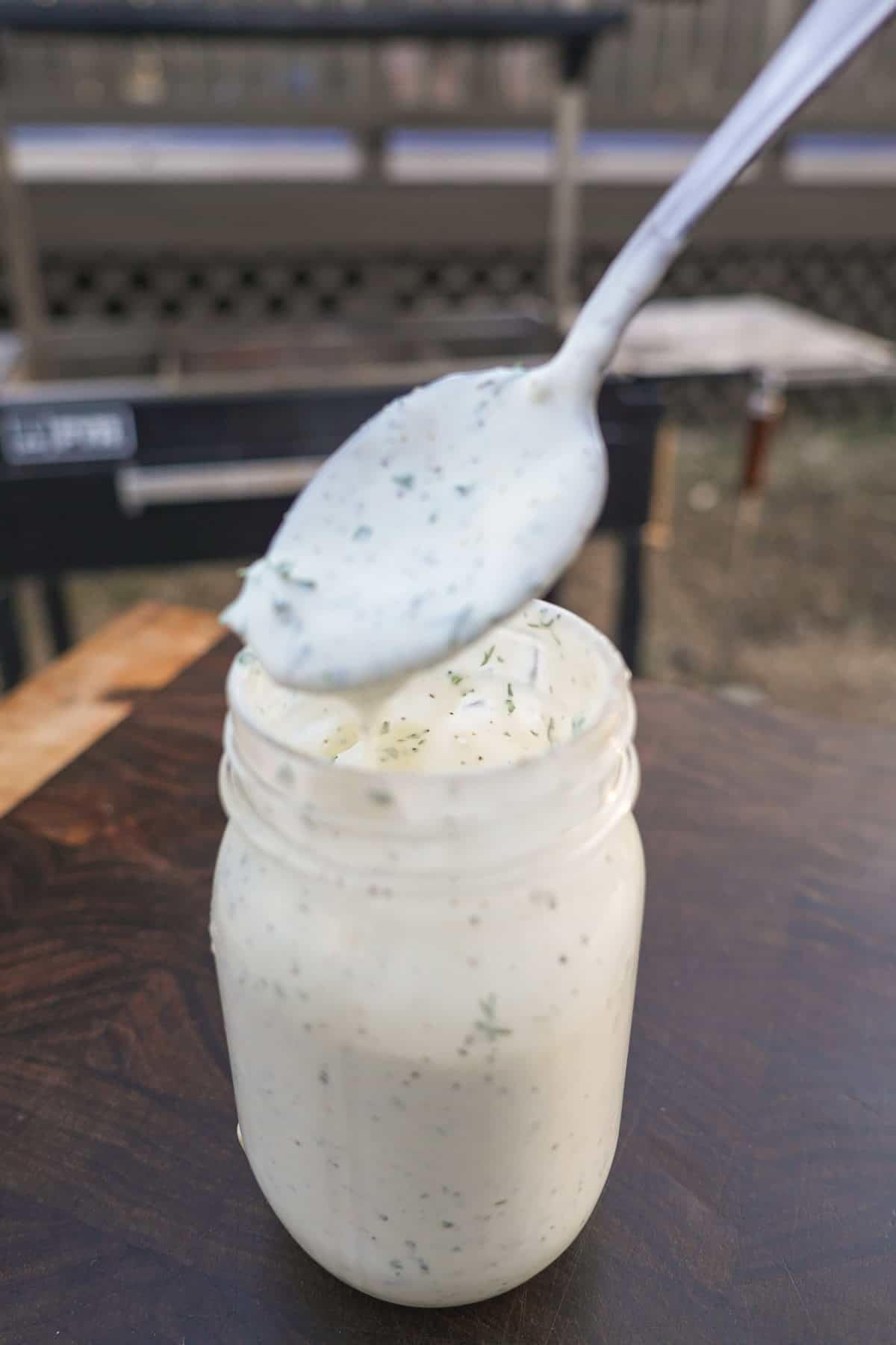 Mixing together ingredients for homemade ranch dressing in a mason jar and holding up a spoonful of the dressing to show texture