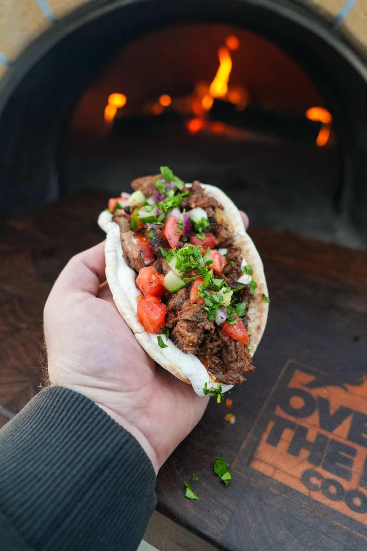 Derek Wolf holding beef shawarma assembled in a pita with tomato cucumber salad and yogurt tahini sauce
