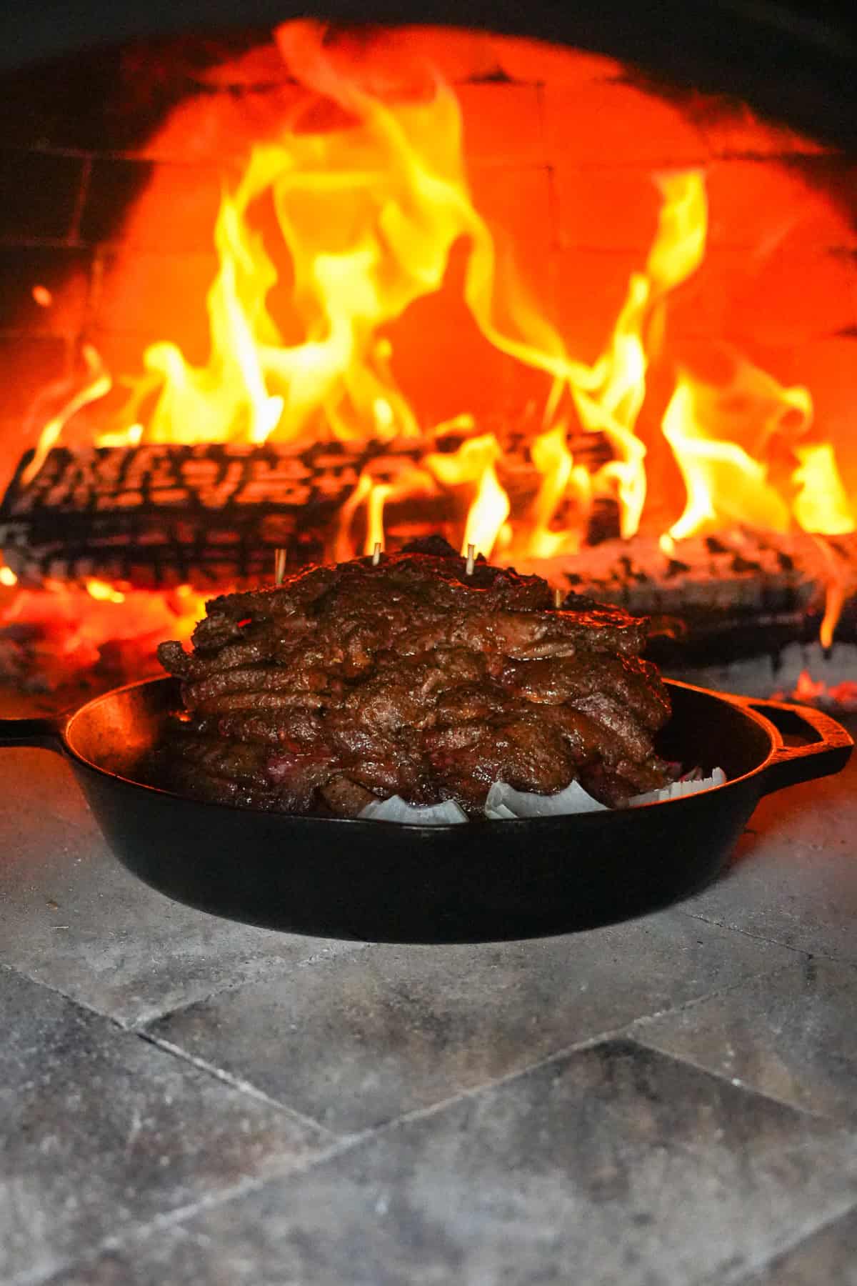 Cooking the stacks of sirloin steak in a cast iron skillet in a flaming pizza oven