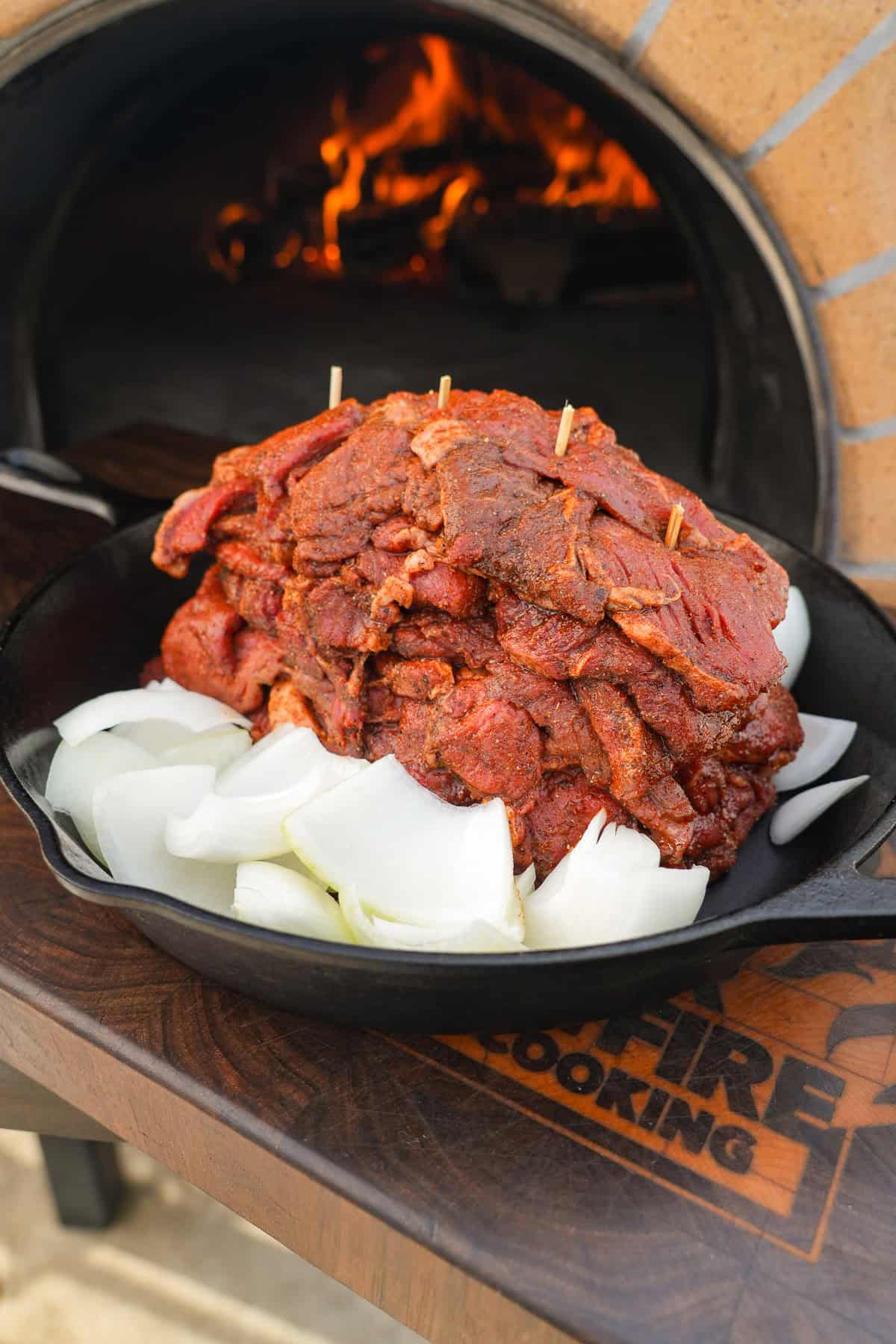Raw sirloin steak seasoned with warm shawarma spices, then placed in a cast iron skillet with raw onions underneath