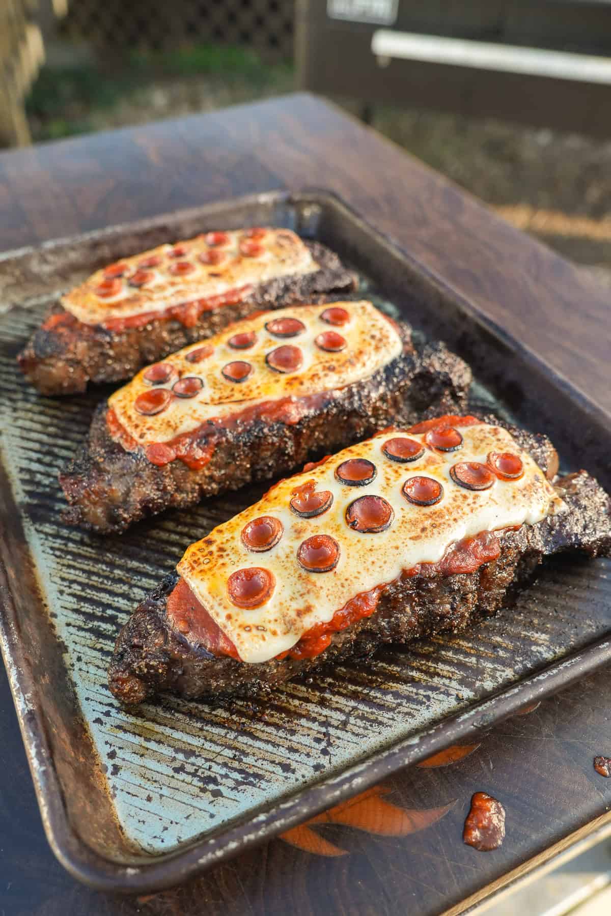 Three pizzas are lined up on the grill, melty, yummy, ready to eat.