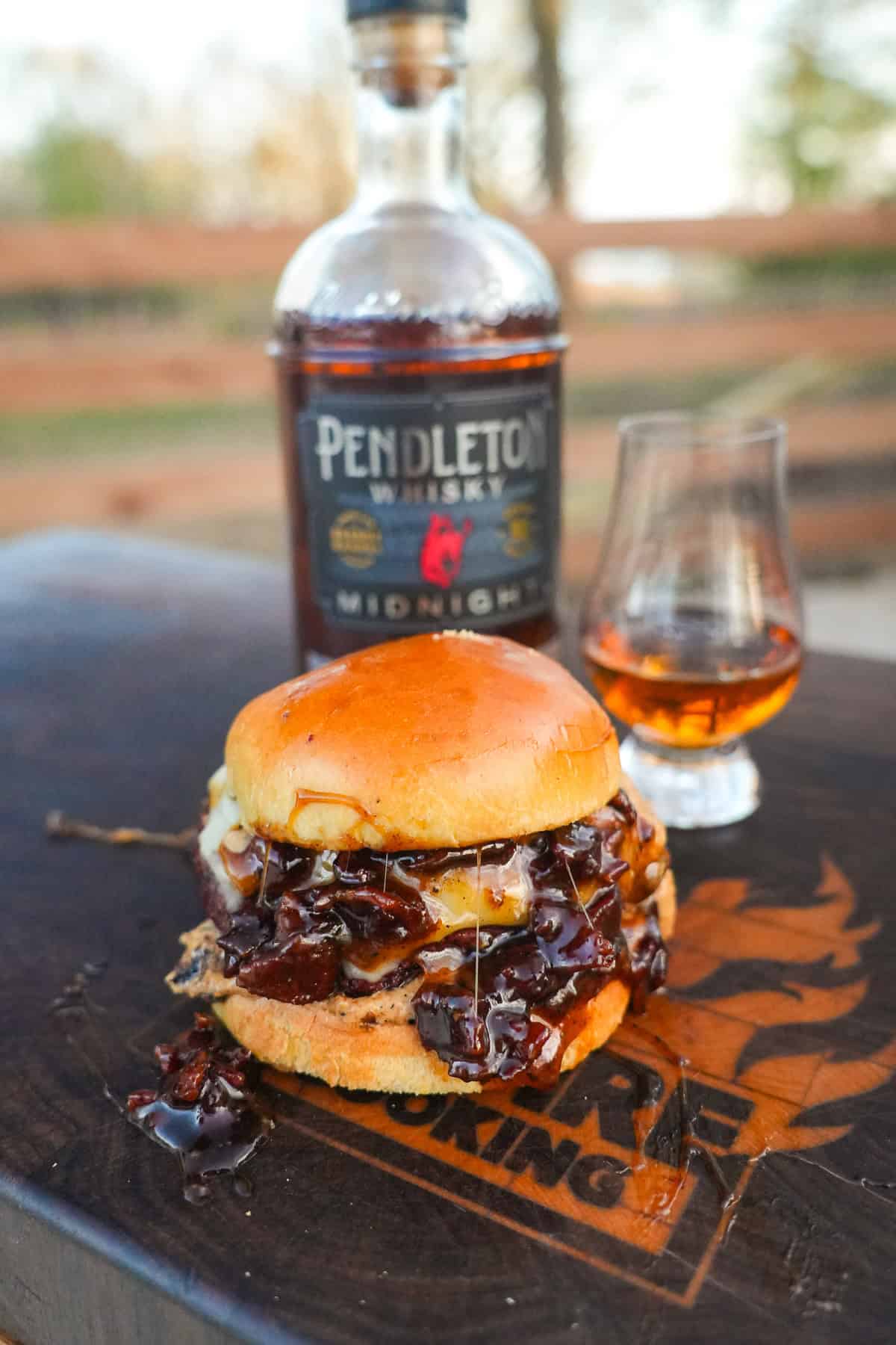 The Whiskey Jam Bacon Burgers recipe cover image features a burger in front of a bottle of whisky.