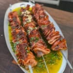 Grilled mortadella skewers atop a platter with Italian chimichurri