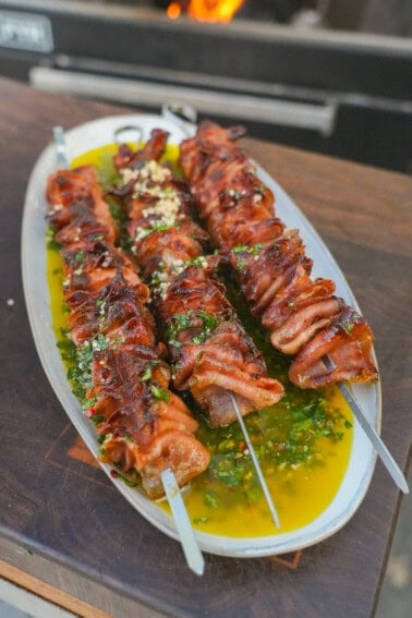 Grilled mortadella skewers atop a platter with Italian chimichurri