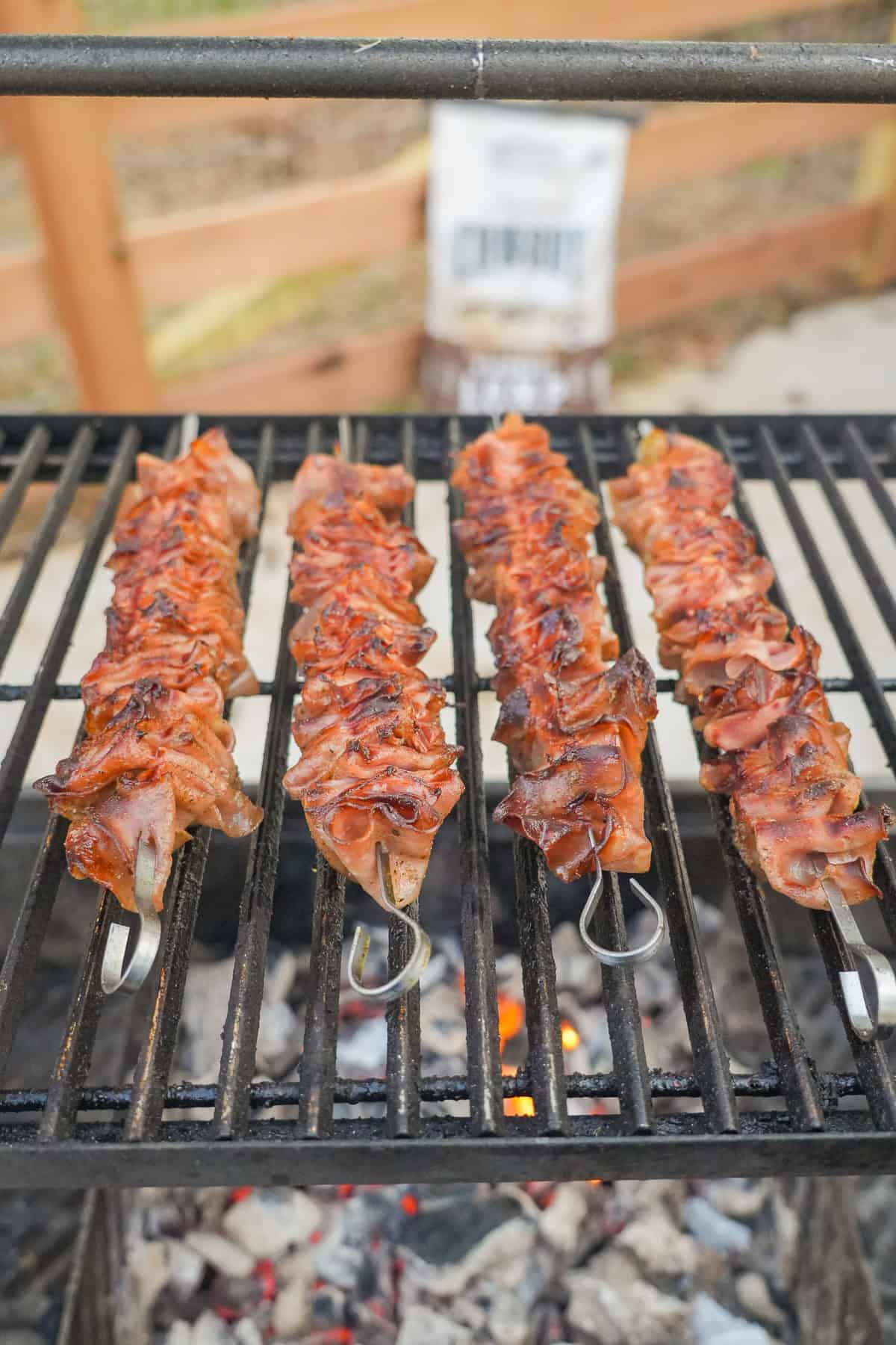 A lineup of four skewers of mortadella on the grill with Cowboy Charcoal as the fuel