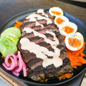 A finished healthy steak bowl with sliced steak, honey chipotle sauce, soft boiled eggs, avocado, pickled red onions and mashed sweet potato