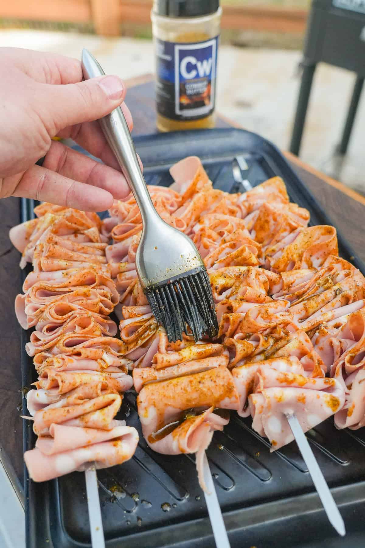 Derek Wolf sticking a fork into an assembled mortadella skewer and seasoning with Cowboy Butter Seasoning
